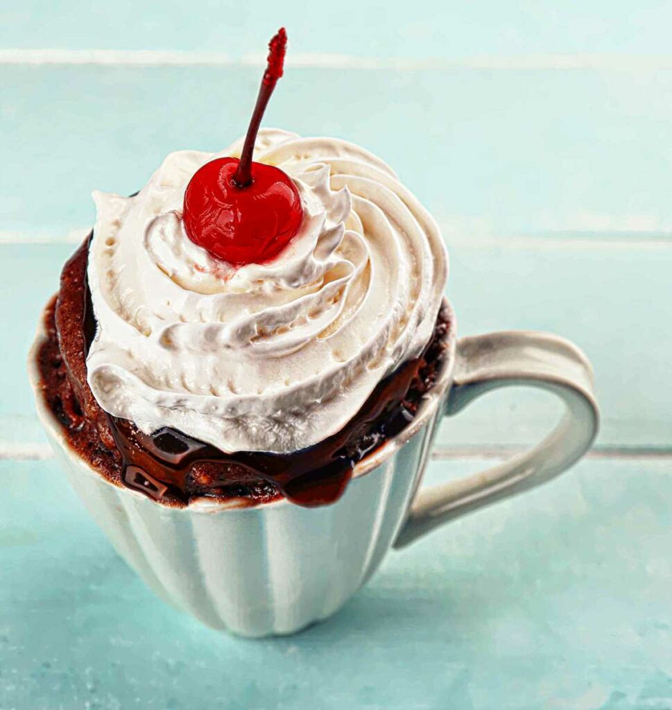 coconut mug chocolate cake topped with whip cream and a cherry